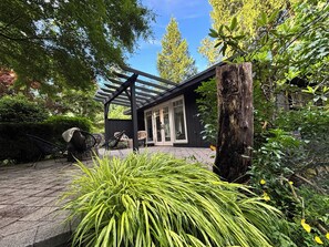 A covered outdoor seating area with chairs, a pergola, and a view of a house with a glass door.
