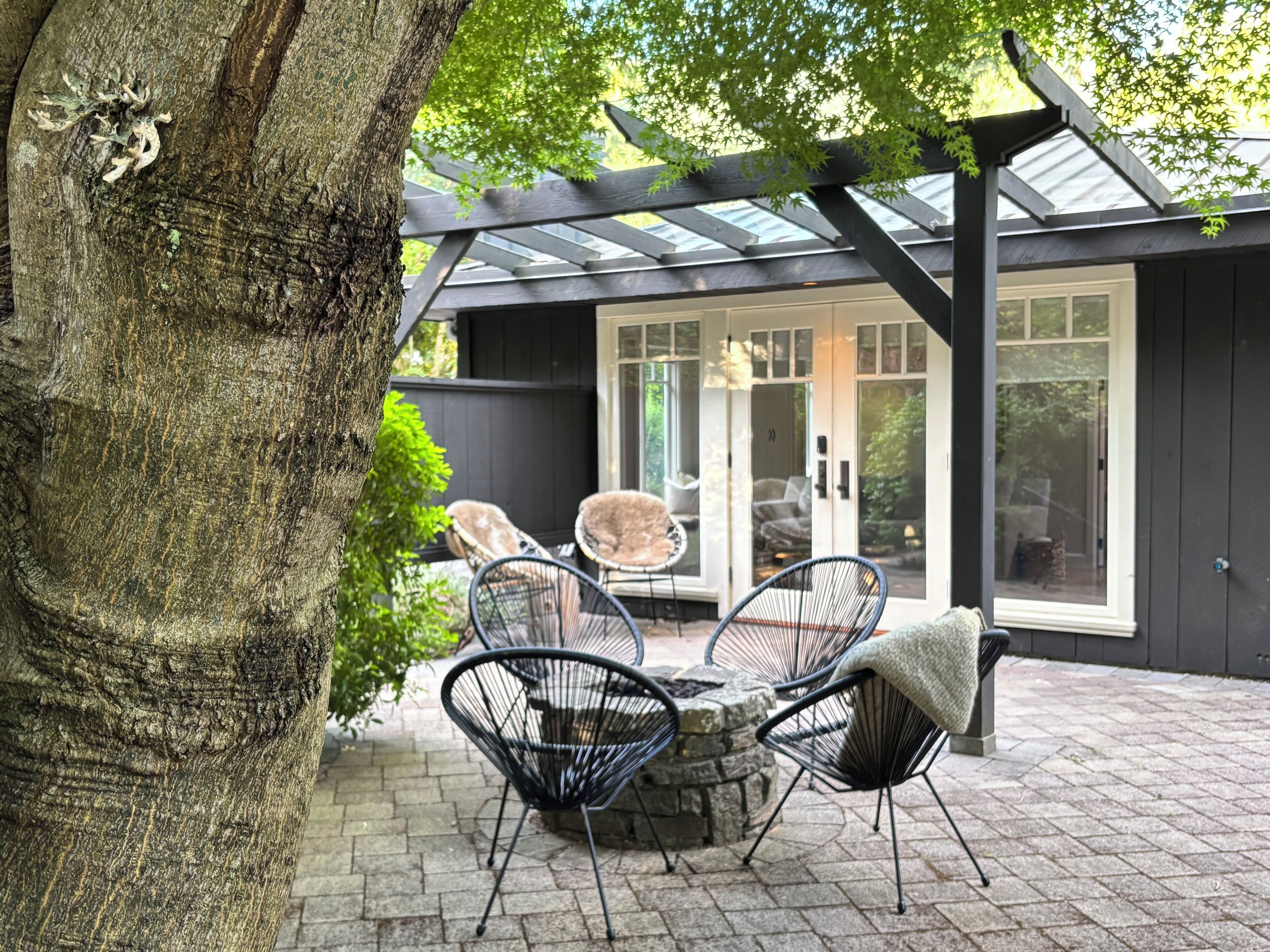 A patio area with stone flooring, a stone fire pit, and black wireframe chairs.