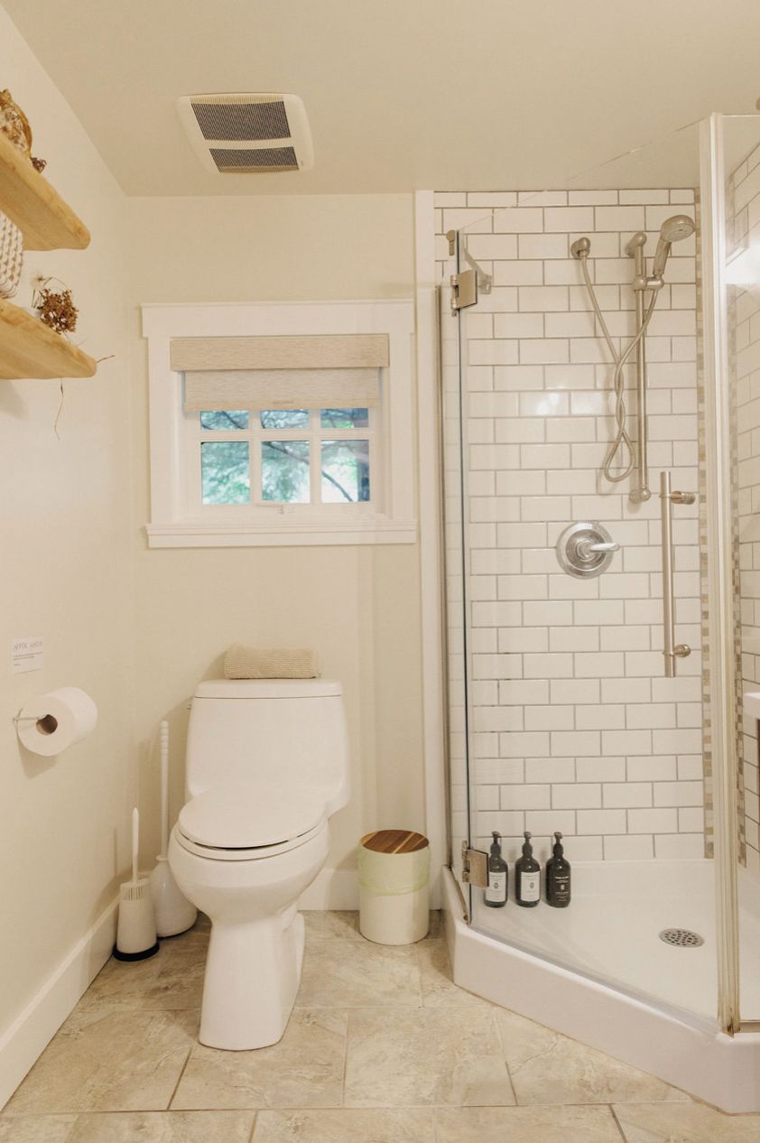 A bathroom with a toilet, a window, a shower, and a toilet paper holder.