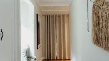 A hallway with wooden flooring, a beige rug, a framed picture on the wall, and a curtain at the end.