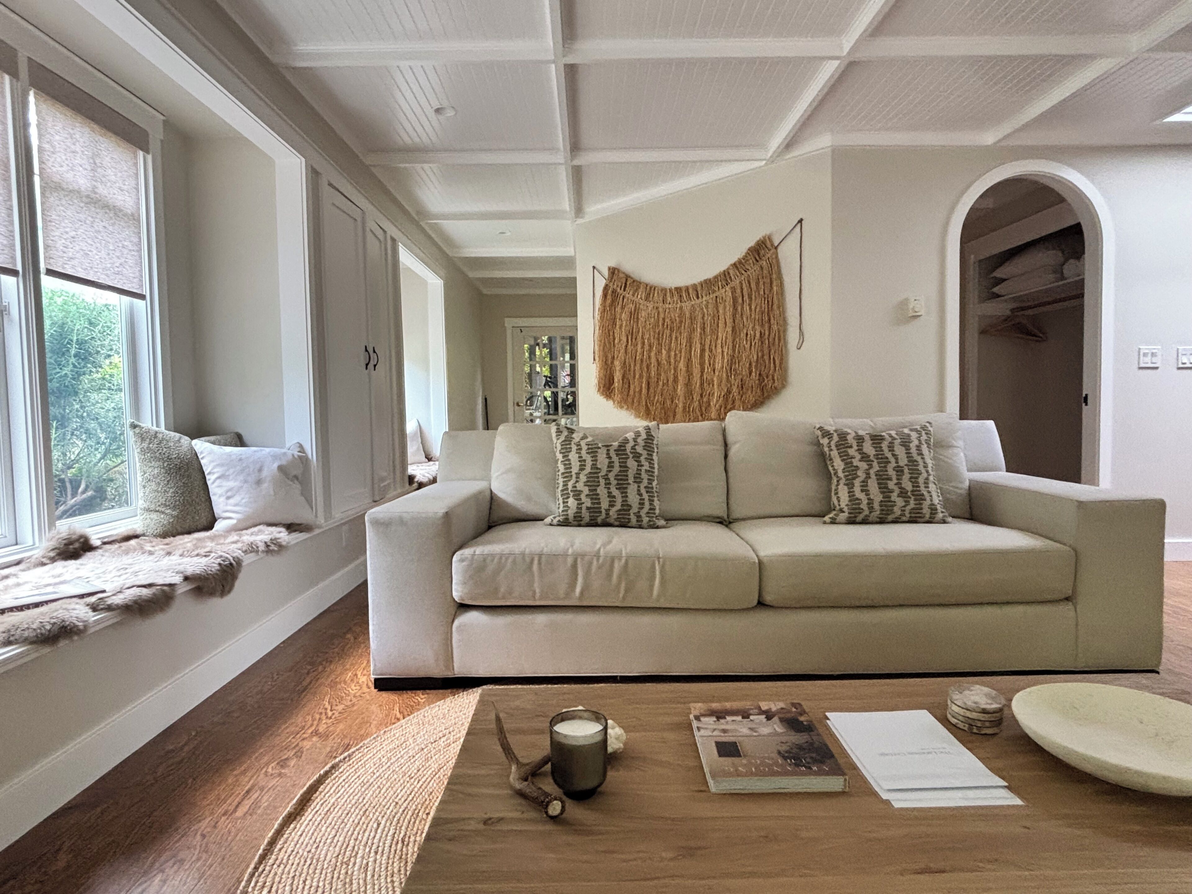 A living room with a sofa, a coffee table, and a view through a window.