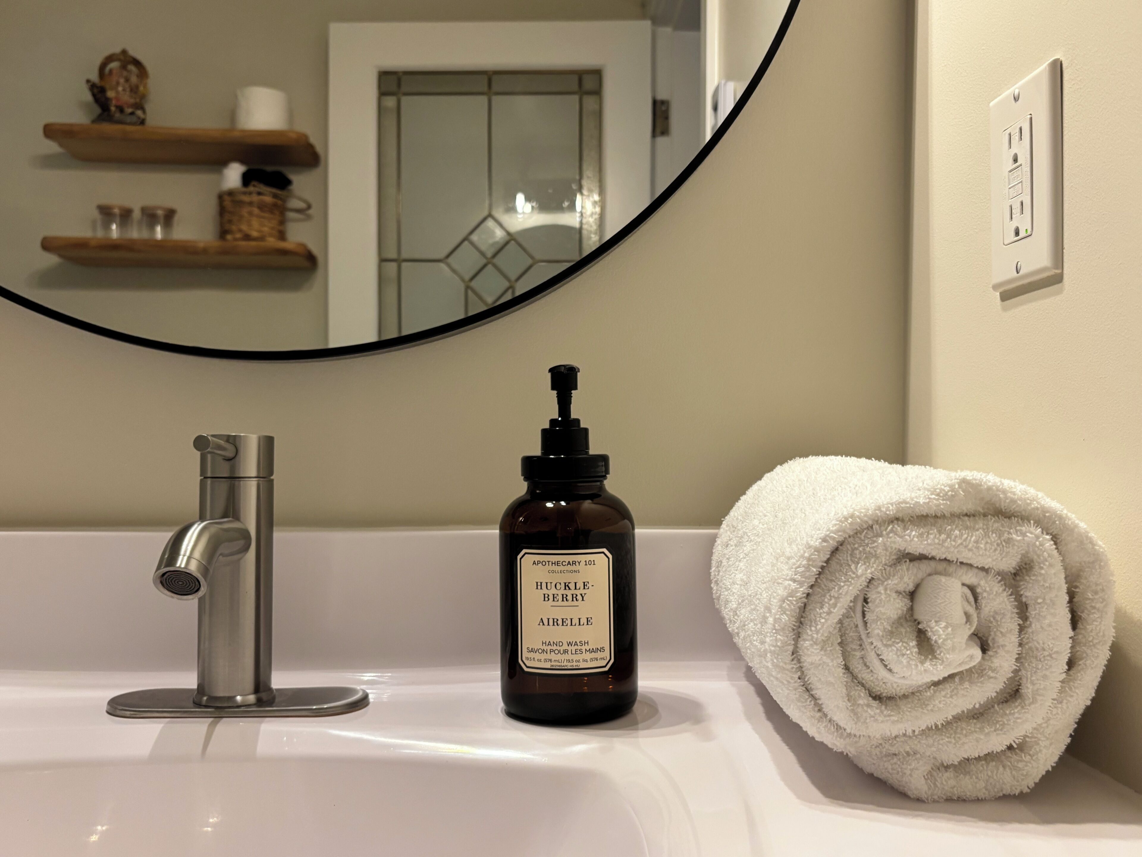 Un lavabo da bagno con un rubinetto moderno, una bottiglia di sapone per le mani e un asciugamano bianco arrotolato.