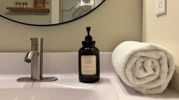 Un lavabo da bagno con un rubinetto moderno, una bottiglia di sapone per le mani e un asciugamano bianco arrotolato.