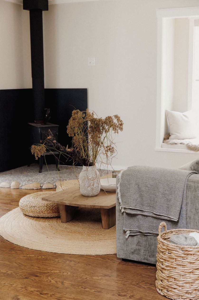 Un salon chaleureux avec une cheminée, un canapé gris, un tapis tissé et une petite table décorée de fleurs séchées.
