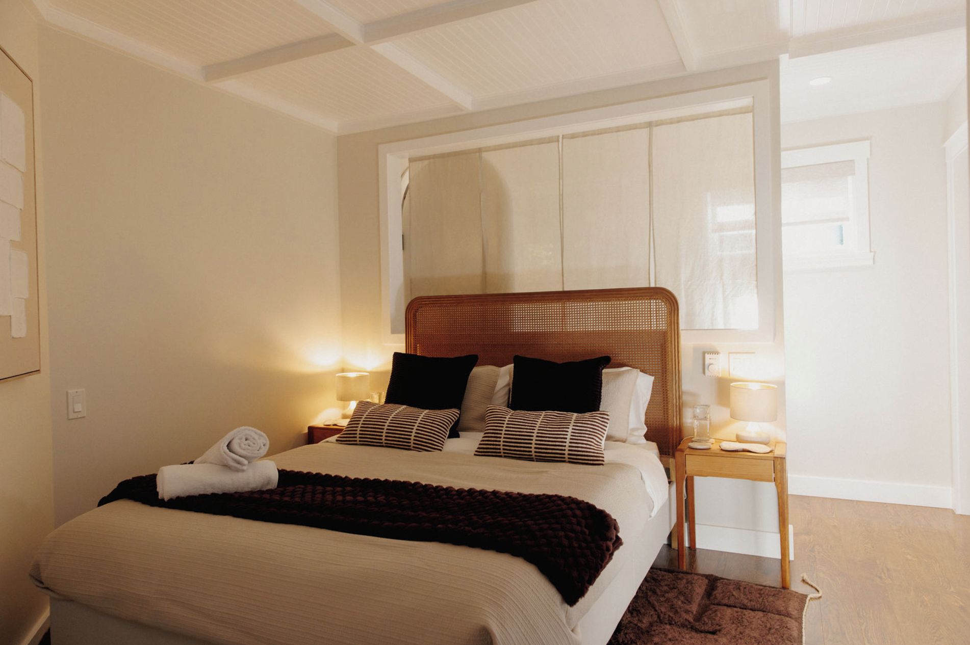 A hotel room with a bed, a nightstand, a lamp, and a window.
