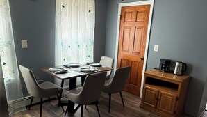 A dining area with a wooden table set for four, four chairs, a wooden cabinet with a coffee maker, and a door with a traditional design.
