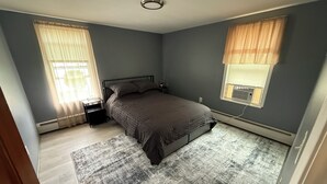 A bedroom with a bed, a nightstand, a window with blinds, and a radiator.
