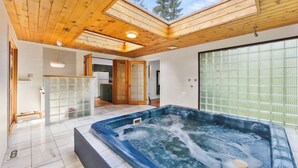 Un bain à remous dans une pièce dotée de poutres apparentes en bois au plafond, d’un coin cuisine et d’une porte-fenêtre coulissante.