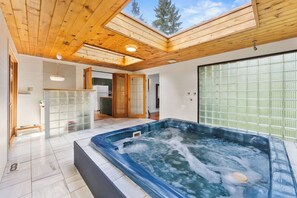 A hot tub in a room with wooden ceiling beams, a kitchen area, and a sliding glass door.