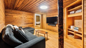 L'intérieur d'une cabane en rondins, avec un canapé, un téléviseur et une bibliothèque.