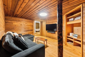 A log cabin interior with a sofa, a television, and a bookshelf.