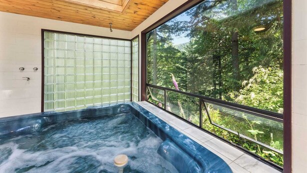 Un bain à remous avec vue sur une forêt, grâce à de grandes fenêtres.