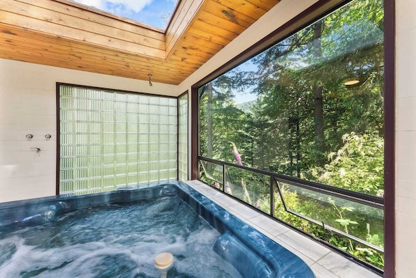 A hot tub with a view of a forest through large windows.