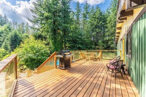 A wooden deck with a grill, chairs, and a view of a forest.