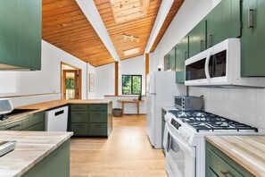A modern kitchen with wooden ceiling beams, green cabinets, a built-in microwave, and a gas stove.