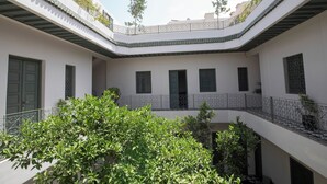A courtyard with a central open space surrounded by buildings, featuring a green tree and a balcony with a railing. - Riad Mudham (Marrakech)