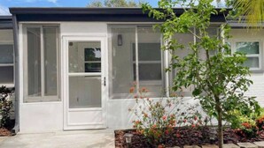 A modern house with a white exterior, a glass door, and a small garden with flowers and a tree. - Pool home in Seminole 5miles to beach (Seminole)