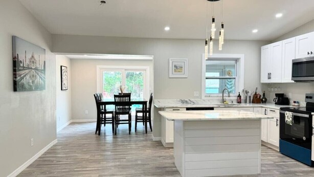 A modern kitchen with white cabinetry, a central island, and a dining area with a table and chairs. - Pool home in Seminole 5miles to beach (Seminole)