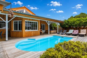 A wooden deck with a swimming pool, lounge chairs, and a covered patio area. - Villa chunga piscine chauffee jacuzzi et clim (Lège-Cap-Ferret)