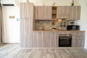 A kitchen with light wood cabinetry, a tiled backsplash, a built-in oven, and a microwave. - GuestHost - Borgo 84 Marzamemi - Happy Family (Pachino)