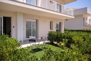 A modern building with a balcony, a patio with a table and chairs, and well-maintained greenery. - GuestHost - Borgo 84 Marzamemi - Happy Family (Pachino)