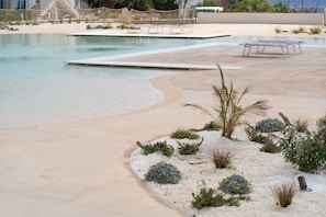 A pool area with a sandy beach, lounge chairs, and a small garden with various plants. - GuestHost - Borgo 84 Marzamemi - Happy Family (Pachino)