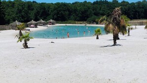 Een strand met een zwembad, palmbomen en bebossing in de verte.