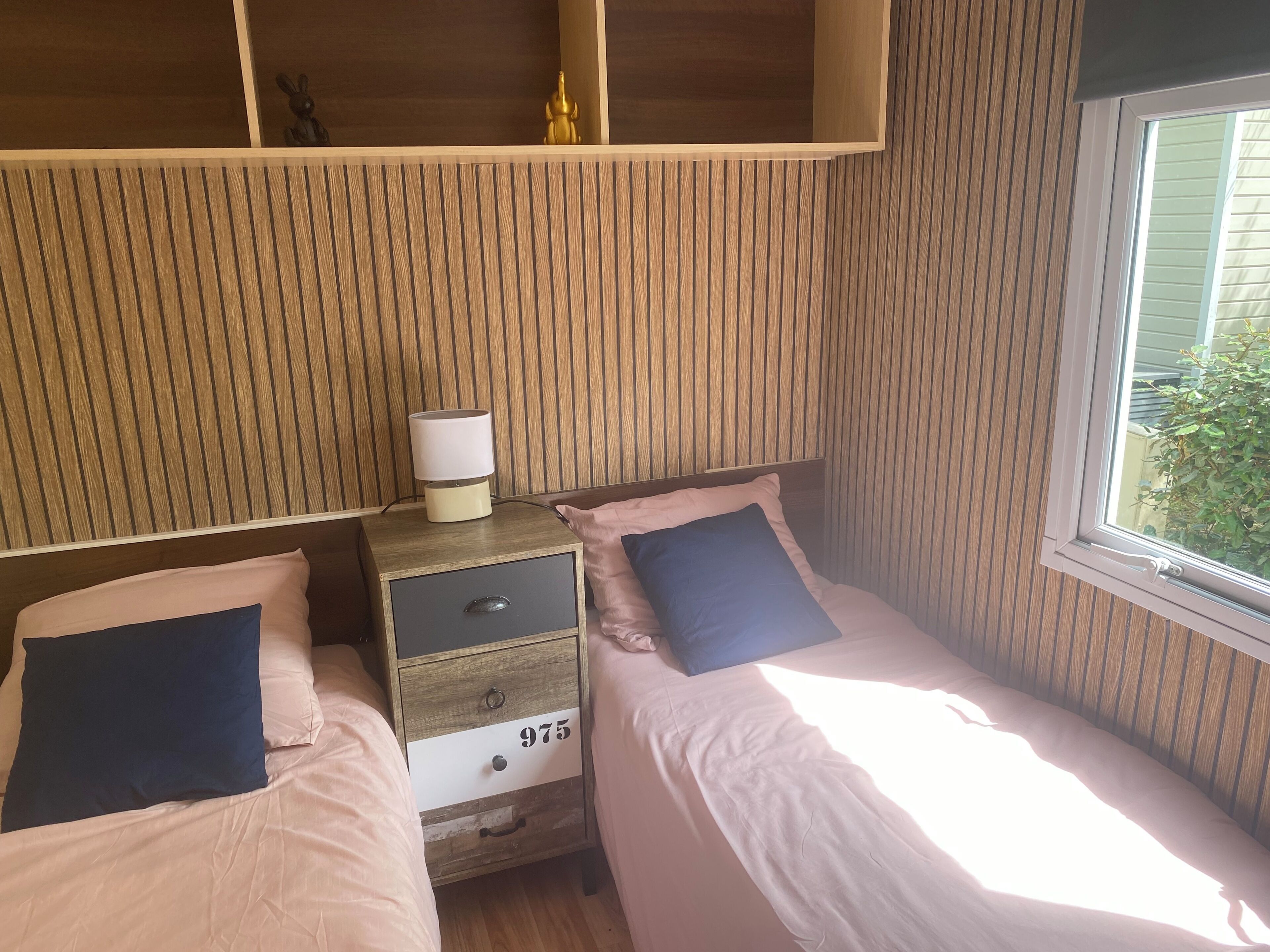 A bedroom with two single beds, a nightstand with a lamp, and a wooden headboard.