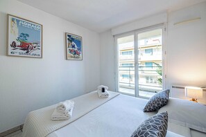 A hotel room with two beds, a window with a view of buildings, and two posters on the wall. - Cozy Apartment Parking & Terrace 1br/4p - Cannes (Cannes)