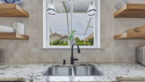A kitchen with a double sink, wooden shelves, a window with a view, and pendant lights. - Beach house|Private Splash Pool|Sleeps 12|Walk to beach|Golf Cart Options (Destin)