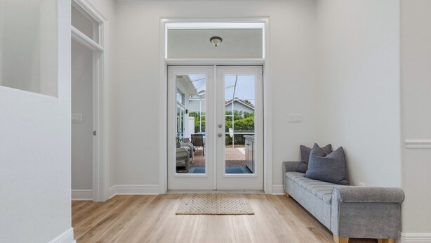 A hallway with a wooden floor, a gray sofa with cushions, and a double door leading outside. - Beach house|Private Splash Pool|Sleeps 12|Walk to beach|Golf Cart Options (Destin)