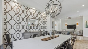 A modern dining area with a white table, black chairs, and a chandelier. - Beach house|Private Splash Pool|Sleeps 12|Walk to beach|Golf Cart Options (Destin)