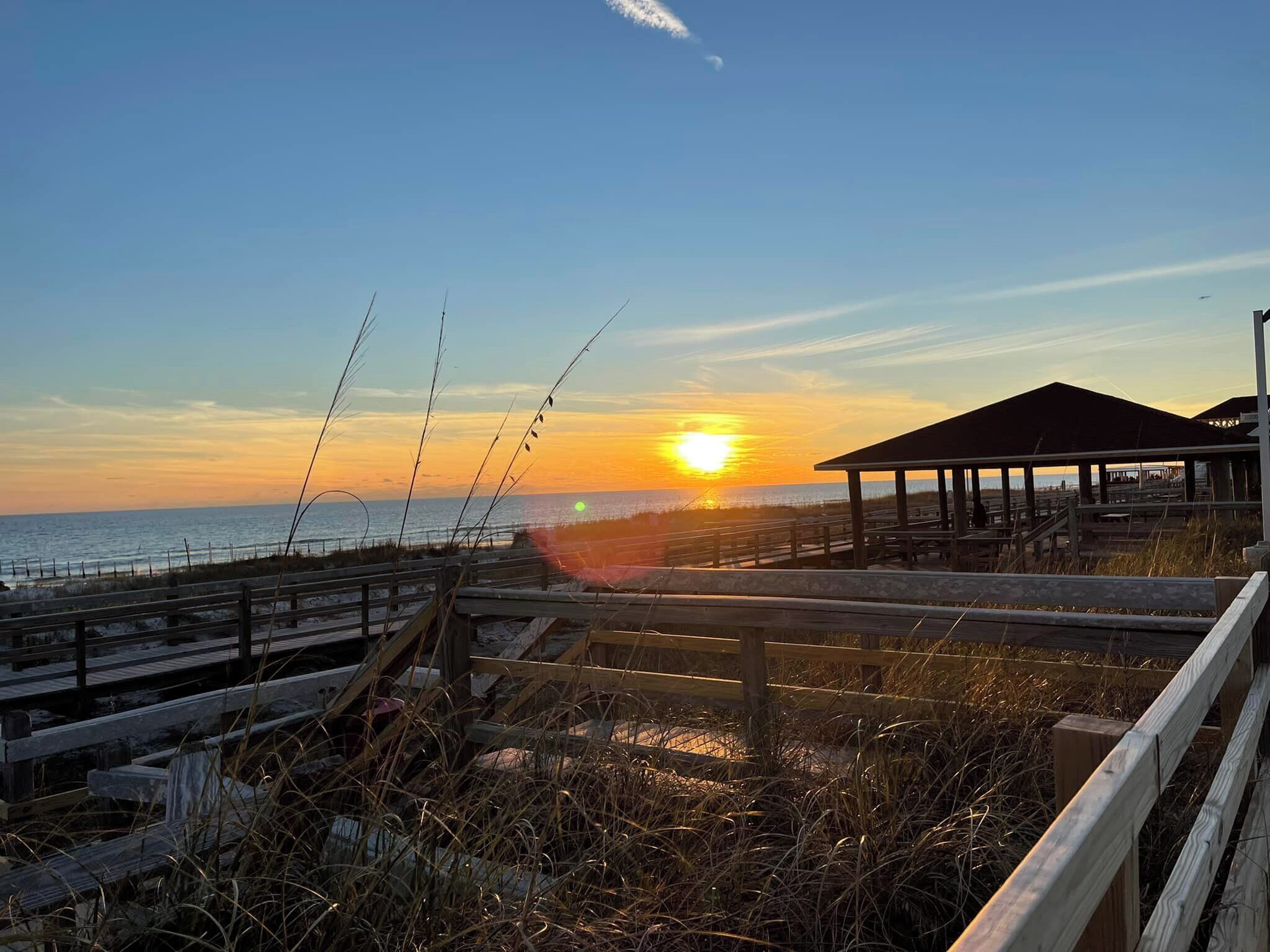 A wooden boardwalk leading to a beach with a sunset in the background.