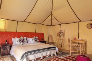A tented room with a bed, bedside tables, a chair, and a small table with a lamp.