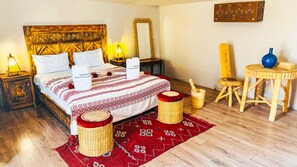 A traditional room with a bed, wooden nightstands, a red patterned rug, a wooden chair, a blue vase, and a wooden table. - Sanmao desert luxury camp,Fantastic 20-bedroom campground in peaceful Merzouga (Merzouga)