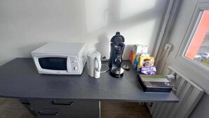 Eine Küchenzeile mit einer Mikrowelle, einer Kaffeemaschine und Kaffeekapseln auf einer Arbeitsplatte.