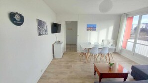 Ein modernes Wohnzimmer mit Sofa, Couchtisch, Esstisch mit Stühlen, Flachbildfernseher und Kunstwerken an den Wänden.