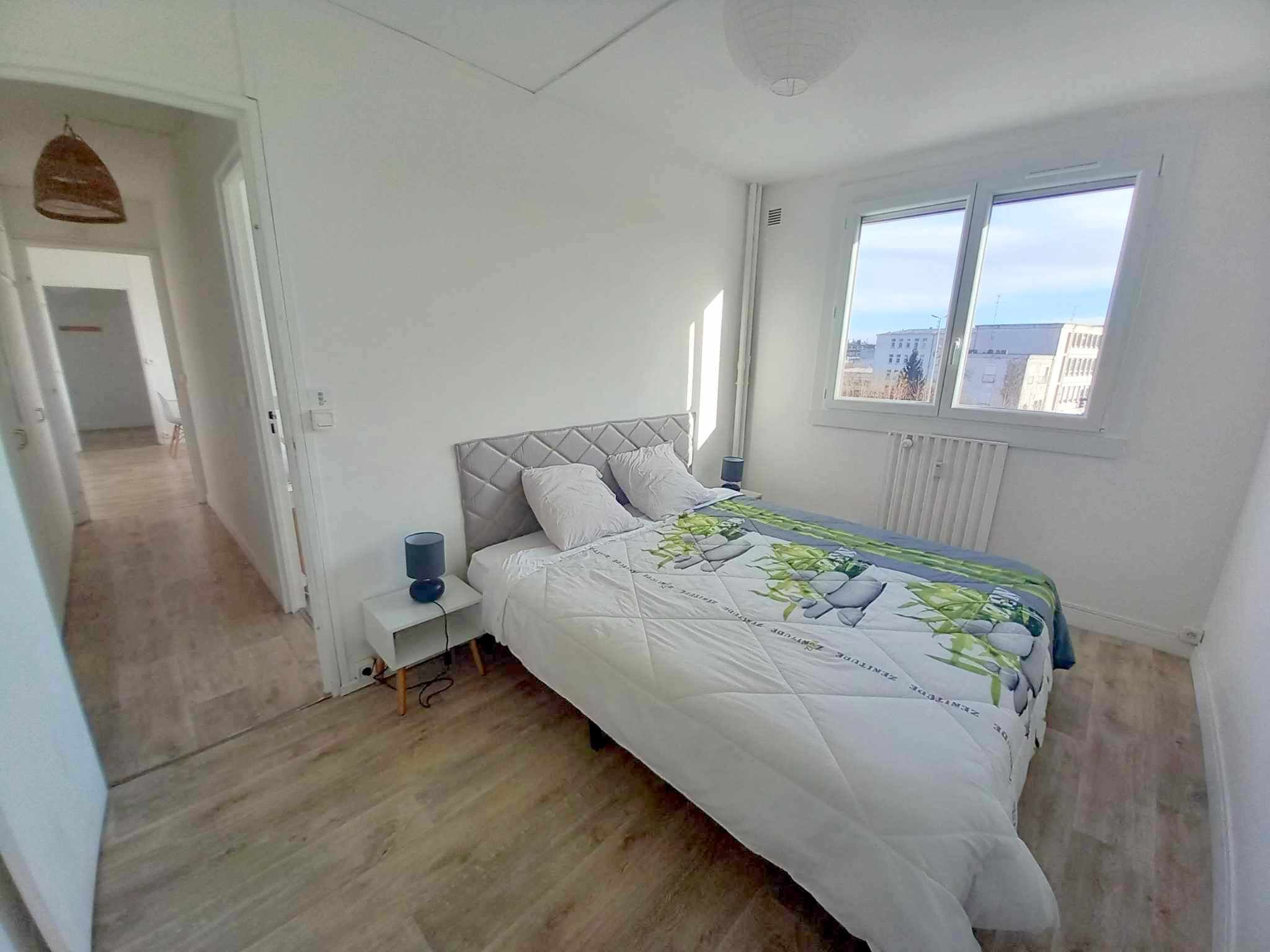 Un dormitorio con una cama, una mesita de noche, una ventana y una puerta que da a otra habitación.