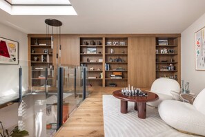Un salon moderne avec une balustrade en verre, une bibliothèque en bois, une table basse ronde et un canapé blanc.