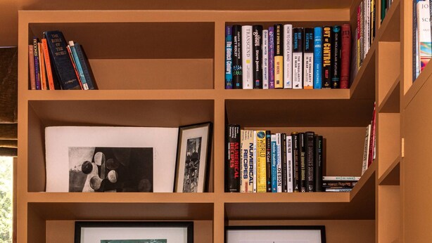 Ein Bücherregal mit verschiedenen Büchern, gerahmten Bildern und einem Schreibtisch mit einem Stuhl.