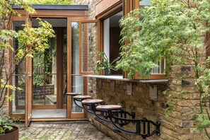 A stone building with a wooden door, a glass door, and a small outdoor seating area with stools. - Elgin Corner by onefinestay (London)