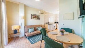 A compact living space with a sofa, a dining table, a kitchen area, and a flat-screen TV mounted on the wall. - Los Boliches Rooftop Retreat • 1BR Sleeps 3 - Pass the Keys (Fuengirola)