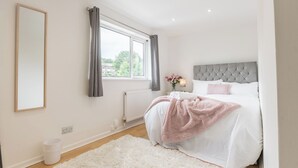 A bedroom with a bed, a window with curtains, a radiator, and a white rug. - 4-Bedroom Home | Sleeps 10 | Parking | Garden - Pass the Keys (Basildon)