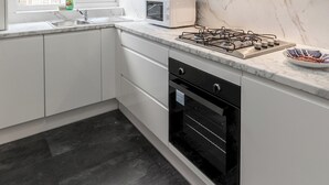 A modern kitchen with white cabinetry, a gas stove, a microwave, and a window with a view of the outside. - 4-Bedroom Home | Sleeps 10 | Parking | Garden - Pass the Keys (Basildon)