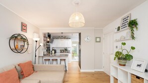 A modern living room with a sofa, a coffee table, a kitchen in the background, and a hallway leading to a door. - Modern Family House | Sleeps 5 | Free Parking - Pass the Keys (Edinburgh)
