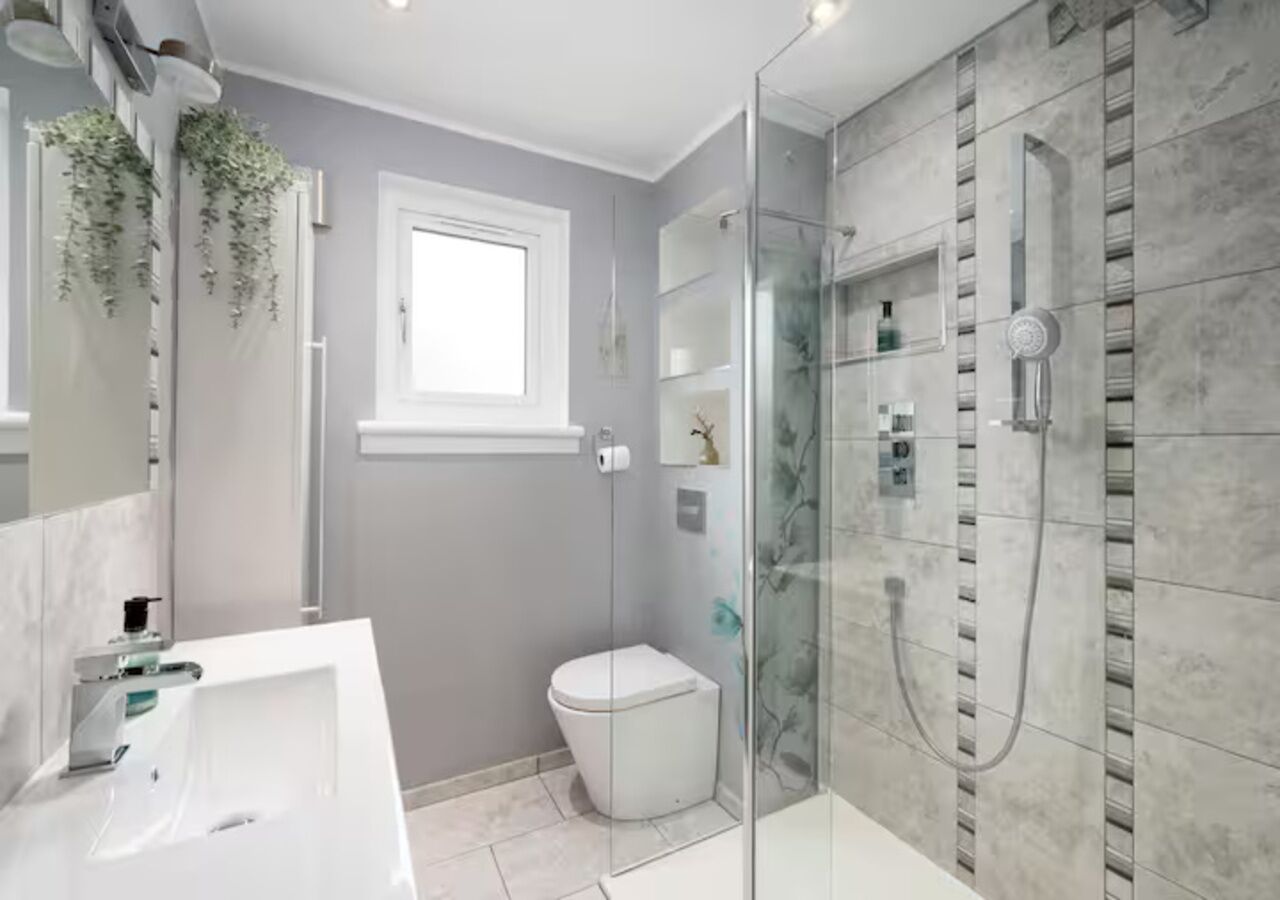 A modern bathroom with a glass shower enclosure, a white sink, and a toilet.