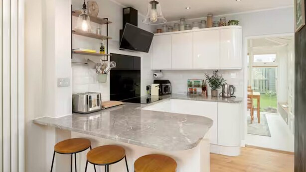 A modern kitchen with a central island, bar stools, a flat-screen TV, and a dining area visible through an open door. - Modern Family House | Sleeps 5 | Free Parking - Pass the Keys (Edinburgh)
