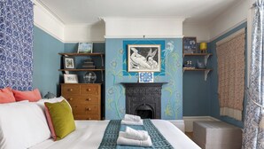 A bedroom with a bed, a fireplace, a shelf with framed pictures, and a patterned wall. - Charming Georgian Retreat | Walk to Beach & City - Pass the Keys (Brighton)