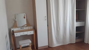 Quarto com toucador de madeira, um banco branco, guarda-roupa branco e cortina branca.