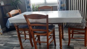 Uma mesa de jantar com quatro cadeiras de madeira, toalha branca e uma cortina estampada ao fundo.